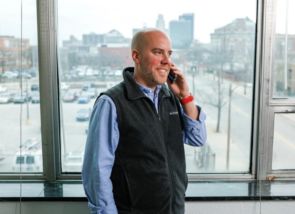 Man on the phone smiling standing in front of windows