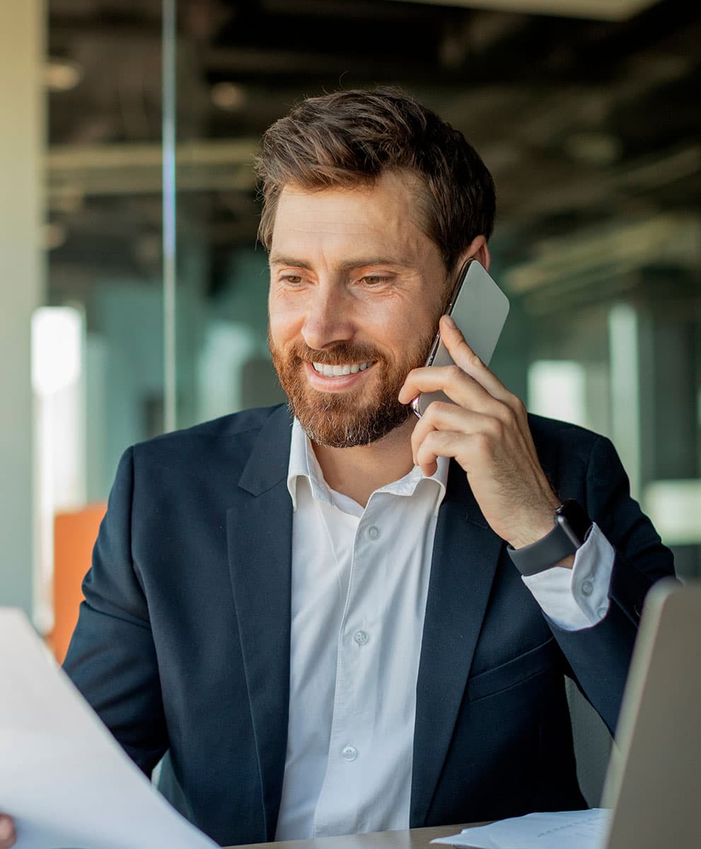 Happy male manager working remotely, reading a financial document and talking on a phone