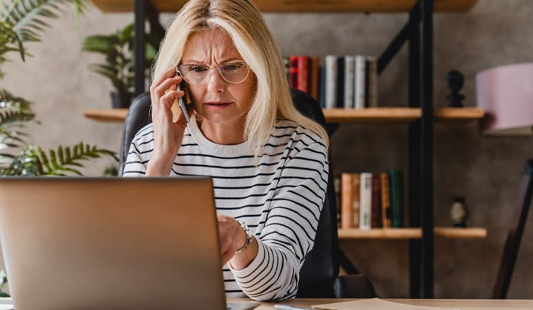 Mature woman looking stressed while using laptop and talking on mobile phone