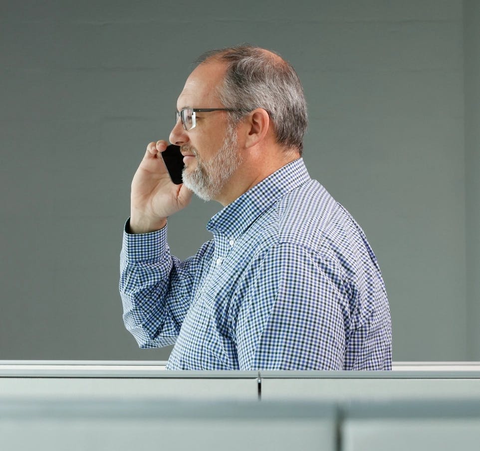 Banner image of a man waling through an office smiling while on the phone