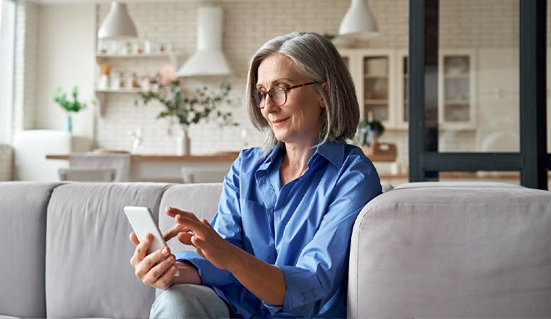 Mature old senior woman using smartphone sitting on sofa at home.